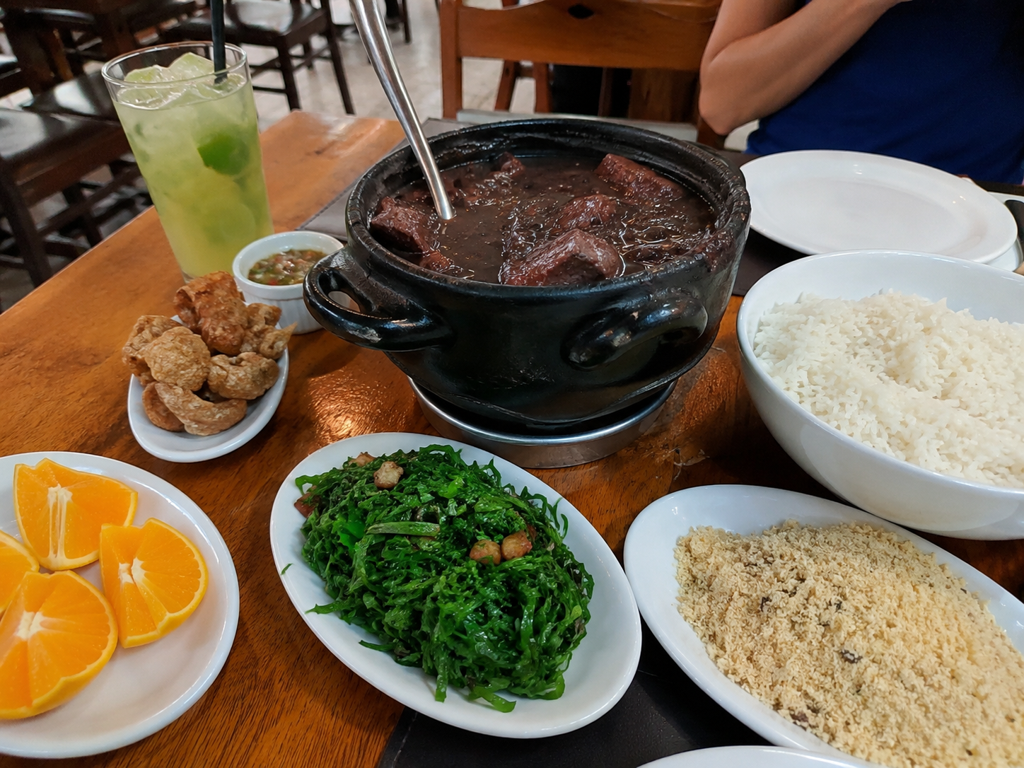 Feijoada tradicional da gastronomia carioca servida em restaurante no Rio de Janeiro, acompanhada de arroz, couve, farofa, torresmo, laranja e caipirinha.