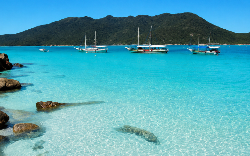 Praia de Arraial do Cabo no Rio de Janeiro com mar azul cristalino, areia branca e barcos na paisagem